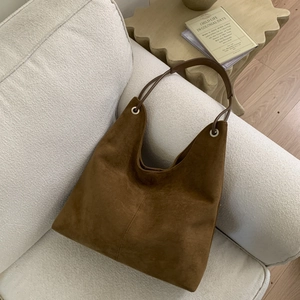 Close-up of brown suede hobo bag with leather straps on a minimalist sofa background