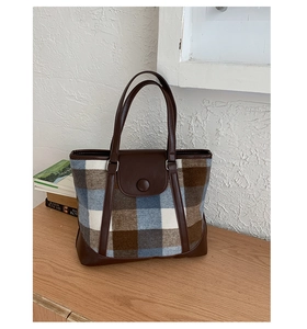 Detail of vintage plaid wool tote bag with brown faux leather trim on wooden surface