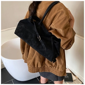 Detail of black suede hobo bag featuring metal buckle and long shoulder strap
