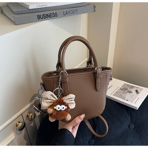 Brown lychee leather handbag with furry monster charm on blue velvet cushion scene