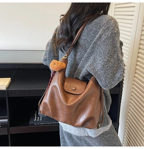 Detail of brown leather tote bag featuring a cute plush bear charm and embossed logo