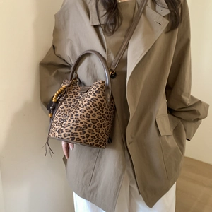 Close-up of leopard print bucket bag with leather handles and tassel charms on model
