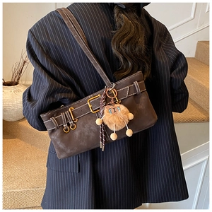 Detail view of brown suede shoulder bag with gold hardware and plush charm on a model