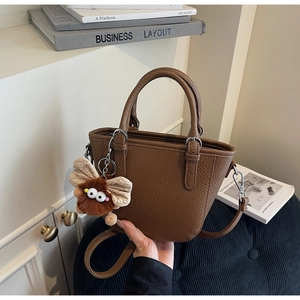 Brown litchi grain leather bucket bag featuring a cute plush doll charm and strap