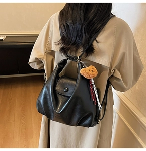 Close-up of black soft pleated leather shoulder bag with a cute brown bear charm