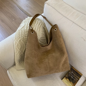 Detail of a large brown suede shoulder bag with vertical stitching on a cozy sofa