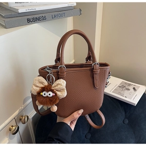 Brown lychee texture handbag featuring a detachable strap and a plush monster charm