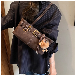 Detail of dark brown suede shoulder bag featuring gold buckles and a cute plush charm