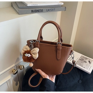 Detail shot of a dark brown lychee leather tote bag with a cute plush monster charm