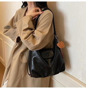Detail of black leather tote bag with embossed logo and brown bear plush charm