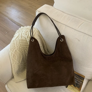 Detail of deep brown suede tote bag with metal ring on a soft fabric sofa