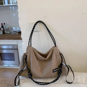 Macro detail of khaki nylon shoulder bag with woven rope handle leaning on white wall