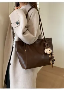 Détail d'un grand sac cabas marron foncé avec pendentif ours en peluche sur manteau