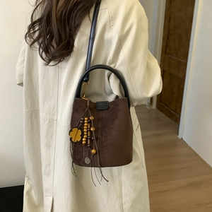 Detail of a brown frosted suede bucket bag featuring black handles and a floral tassel charm