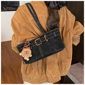 Detail of black matte shoulder bag with white contrast stitching and plush bear charm