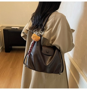 Detail of dark brown glossy leather tote bag with embossed text and plush bear charm