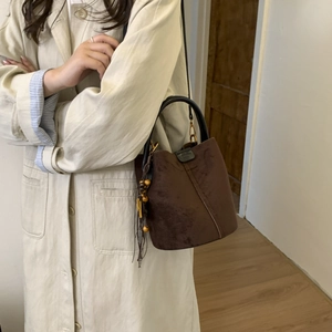 Close-up of vintage brown suede bucket bag featuring contrast stitching and tassel detail