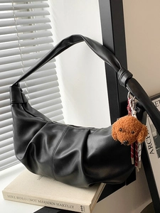 Black pleated faux leather shoulder bag with plush dog charm on a decorative book