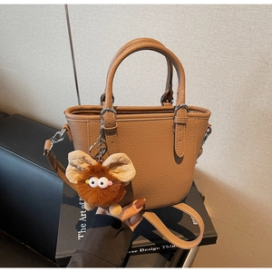 Detail view of brown pebbled leather handbag with double handles and plush monster charm