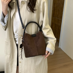 Detail of vintage matte brown suede bucket bag with black leather handle and side tassel