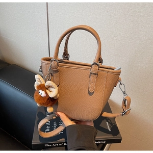Close-up of brown litchi pattern handbag with plush charm and detachable shoulder strap
