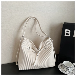 Detail of cream pleated tote bag with metal buckle and vertical folds in a studio setting