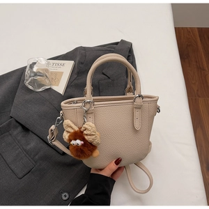 Detail of beige textured leather handbag with a plush brown monster charm on a grey blazer