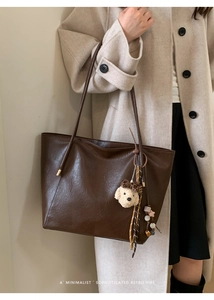 Détail d'un cabas en cuir marron foncé avec bandoulière et pendentif chien en peluche