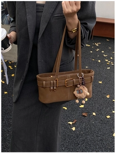 Close-up of retro brown shoulder bag with decorative buckle and plush pendant charm