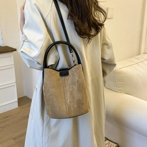 Close-up of brown matte bucket bag with black leather straps and gold metal hardware
