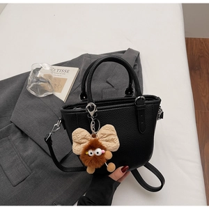 Detail of black litchi pattern handbag with a cute plush monster charm on gray blazer