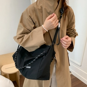 Detail of black nylon crossbody bag with woven rope strap and fashion label on brown coat