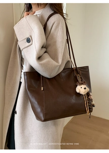 Détail d'un grand sac cabas en cuir marron avec un charme chien en peluche sur un manteau