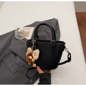Detail of black pebbled leather handbag with plush bow charm on a grey suit background