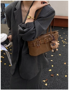 Brown frosted leather shoulder bag with gold buckle and plush bear charm outdoors