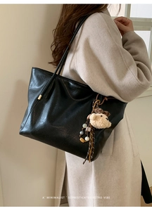 Détail d'un grand sac cabas noir avec pendentif ours porté sur un manteau beige