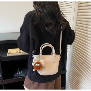 Detail of beige lychee textured mini tote bag with cute brown plush monster charm