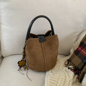 Detail of frosted brown bucket bag featuring black leather handle and floral charm accent