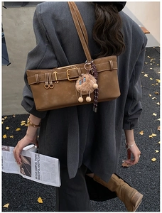 Brown suede shoulder bag with gold buckle and cat charm on a street background
