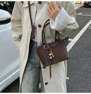 Close-up of dark brown quilted leather bucket bag with metal triangle logo and tassel detail