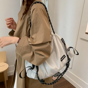 Detail of white crossbody bag with black and white woven rope strap on a model