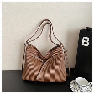 Detail of brown pleated faux leather bag with metal buckle on a minimalist desk