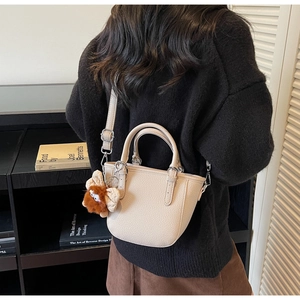 Beige litchi grain mini tote bag with monster charm shown on a crossbody model