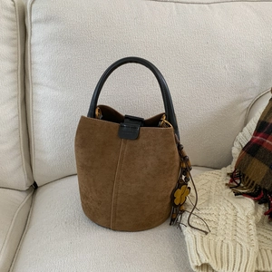 Close-up of brown suede bucket bag with floral charm on white textured background