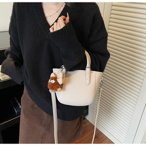Detail of creamy white litchi pattern leather bag with plush bear charm and silver buckle
