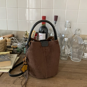 Close-up of brown suede bucket bag with floral charm and black leather handle on wood
