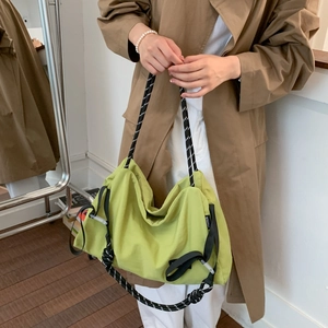 Detailed shot of lime green nylon shoulder bag with woven strap on trench coat model