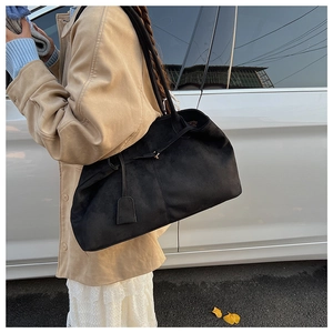 Detail view of large black matte tote bag worn with a chic beige trench coat outdoors