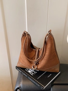 Brown suede tote bag with metal ring detail on a black prop book background