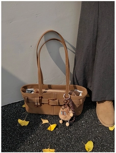 Detail of vintage brown bucket bag with capybara plush charm on ginkgo leaf background